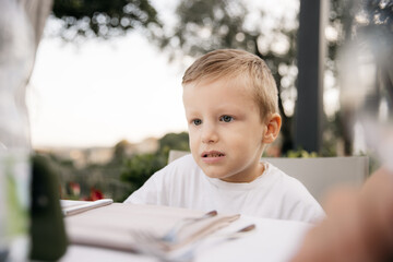 Little boy waiting for food at restaurant table in tuscany