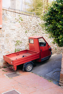 Red three-wheeled ape car parked in narrow tuscan alley