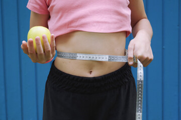 a girl with a measuring tape around her waist holds an apple in her hand