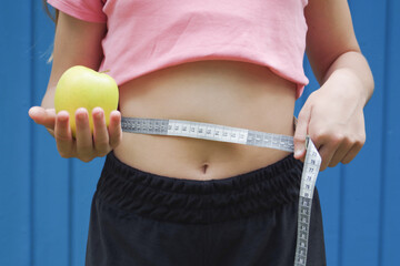 a girl with a measuring tape around her waist holds an apple in her hand