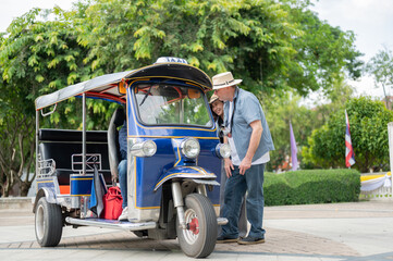Old white man and wife talking to driver after riding in tuk tuk or three wheel taxi touring a city.