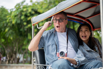Old white man and asian woman looking excited while riding in tuk tuk three wheel taxi touring city