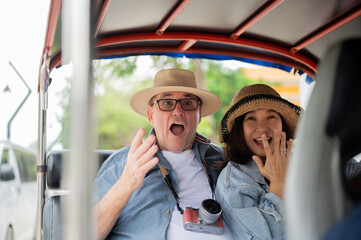 Old white man and asian woman looking surprised as riding in tuk tuk three wheel taxi touring a city