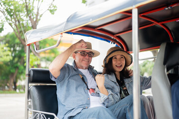 Couple of old white man and asian woman enjoy riding in tuk tuk or three wheeled taxi touring a city