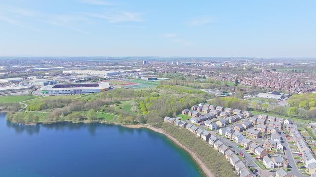 Drone captures calm lake bordered by houses, green parkland, and Doncaster Rovers stadium in Doncaster Lakeside, South Yorkshire, UK, showcasing urban and natural coexistence.