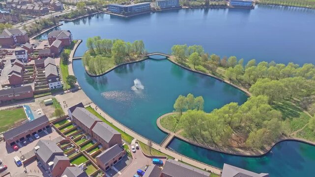Slow drone descent captures Doncaster Lakeside with calm water, curved walking paths, green trees, fountain spray, surrounding residential buildings, and peaceful parkland atmosphere.