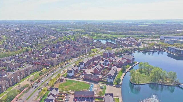 Aerial drone shot glides above Doncaster Lakeside, revealing modern homes, winding roads, blue water, lush trees and expansive cityscape in bright daylight.