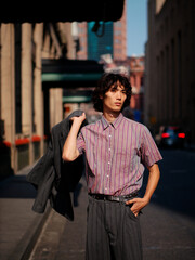 Portrait of handsome Chinese young man wearing stripe shirt posing in the street, young guy with black curly hair with urban background. Male fashion, cool Asian young man lifestyle.