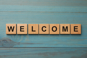 Word Welcome made of wooden cubes on light blue table, top view