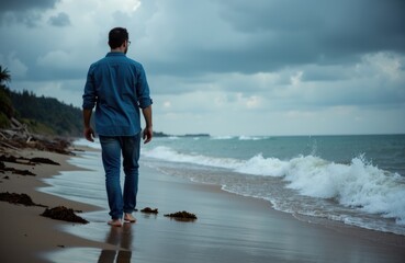 A man walking alone along a cloudy beach shoreline with waves crashing onto the sand