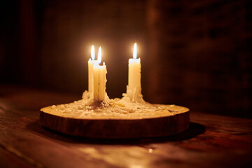 Four lit candles on wooden base illuminate rustic table in dark, cozy and peaceful atmosphere....