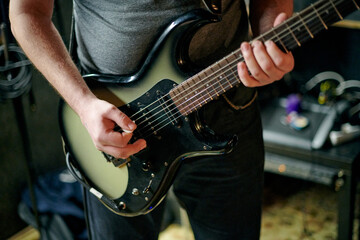 Obraz premium Musician playing an electric bass guitar at music rehearsal, practicing guitar technique in dimly lit setting, close up view guitarist hands