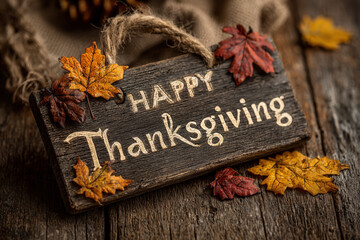 Rustic wooden sign with happy thanksgiving text and colorful autumn leaves
