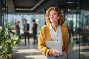 Young professional woman confidently walking with laptop in modern open office