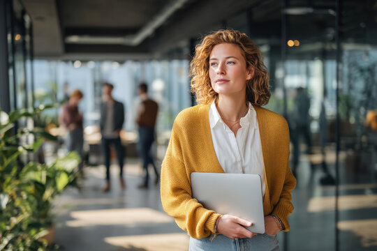 Young professional woman confidently walking with laptop in modern open office