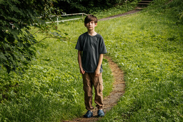 On a summer day, a little boy walks alone along a winding dirt path through a lush, green park...