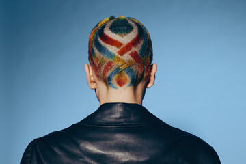 Woman with colorful geometric hair design and shaved head wearing black leather jacket against blue...