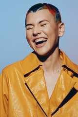 laughing woman with colorful hair and yellow jacket expressing joy and happiness, isolated on blue...