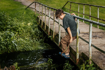 On a quiet summer day, a little boy leans thoughtfully against the rusty metal railing of a small...