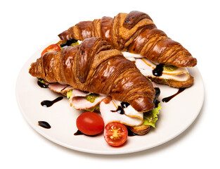 Two freshly baked classic delicious fresh organic croissants with ham, cheese, pesto sauce and tomatoes on a white ceramic plate isolated on white background