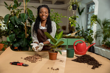 Smiling young woman with dreadlocks plating flowers and looking involved