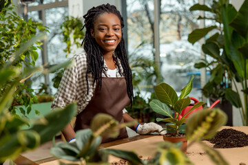 Smiling young woman with dreadlocks plating flowers and looking involved