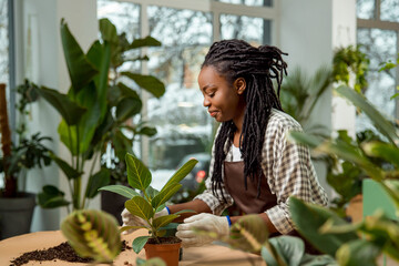 Smiling young woman with dreadlocks plating flowers and looking involved