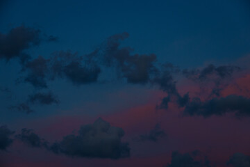 Scattered dark clouds float across a twilight sky bathed in deep blue and delicate pink tones, creating a peaceful and moody scene with copy space.