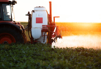 Tractor spraying crops in a lush green field at sunset.