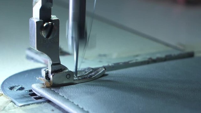 Sewing automated machine stitching gray leather in industrial workshop.