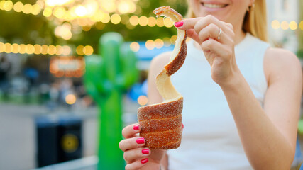 Happy woman with bright pink nails holding a freshly baked cinnamon-sugar coated trdelnik with a...