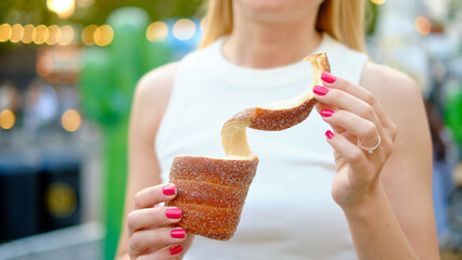 Close-up of a woman with pink nails holding a spiral cinnamon-sugar coated trdelnik pastry during...