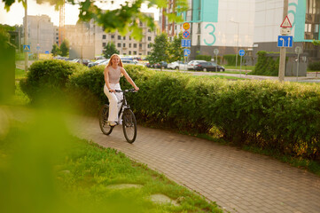 smiling woman riding bicycle on sunny urban path with lush greenery. embracing outdoor lifestyle and healthy activity in modern city setting. ideal for wellness themes and urban living concepts