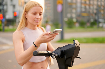 woman using smartphone outdoors with electric scooter. focused young adult navigating city street,...