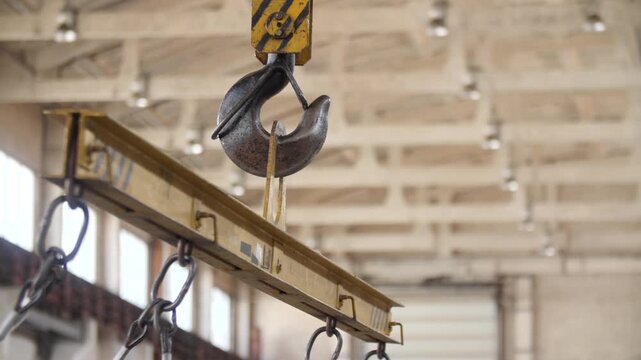 Industrial crane hook hanging in large warehouse in industrial workshop.