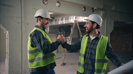 Two happy Caucasian men greeting friends buddies males guys workers in uniform helmets business construction teamwork engineers architects meeting shaking hands building cooperation colleagues gesture