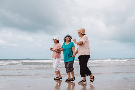 Asian senior women walking and laughing on the beach, representing aging and insurance planning. Embracing retirement security, health, friendship, and carefree living in later life.