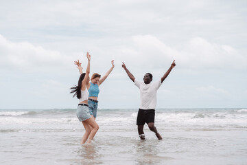 Young diverse friends holding hands and playing together in ocean water on a summer beach. Symbol of friendship, travel, freedom, and fun holiday moments with joy and connection.