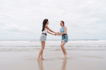 Two young women holding hands and laughing playing on the beach, carefree friendship, freedom, and...