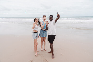 Diverse group of young friends taking selfie and enjoying time together on the beach. Fun summer vacation moment symbolizing friendship, freedom, and multicultural connection.