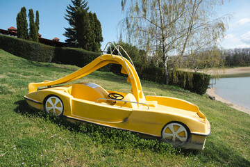 Abandoned yellow pedal boat with a slide, sitting on green grass near a lake. The worn-out...