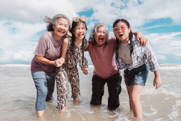 Asian multi generational family enjoying joyful moments on the beach. Happy women and daughter splashing water together, fun, bonding, and freedom across ages.