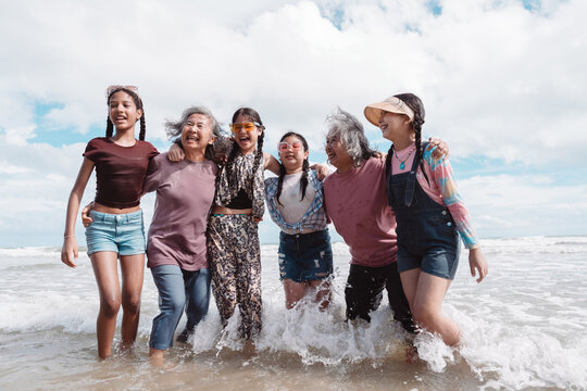 Happy Asian family group, senior women and kids enjoying playful beach. Celebrating love, wellness, and multi generational togetherness by the sea.