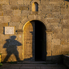 Shadow of a pilgrim with backpack cast on the stone wall of a historic chapel entrance, Camino de Santiago, at golden sunset.