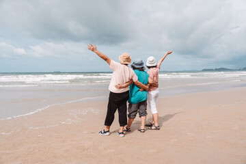 Elderly women embracing and raising arms while enjoying a peaceful beach getaway. Concept of friendship, freedom, relaxation, and joyful retirement lifestyle.