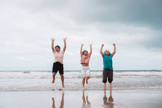 Asian senior females jumping with joy on the beach, expressing freedom, vitality, and happiness in retirement. Ideal for insurance, lifestyle, and retirement planning - Powered by Adobe