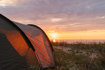 A warm glowing tourist tent on a sandy sea coast, with a beautiful, serene, and scenic sunset over...