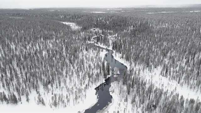 Aerial, forward flight high above a river surrounded by snowy forest