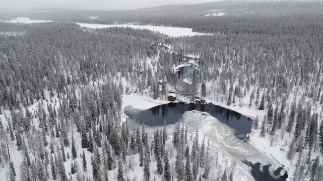 Aerial, descending and tilting up towards a little lake surrounded by snowy forest