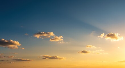 Obraz premium A blue sky transitions to golden sunlight near the horizon with small, puffy clouds scattered throughout